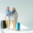 Man and woman elderly couple standing in front of white wall with black and teal suitcases
